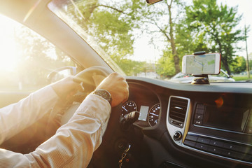 Directions on cell phone in phone holder mount on dashboard dash panel surface, expensive vehicle interior. Gps route navigation concept. Young man hands on steering wheel. Sunset background, close up