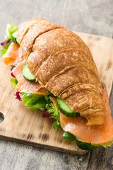 Croissant sandwich with salmon and vegetables on wooden table. 
