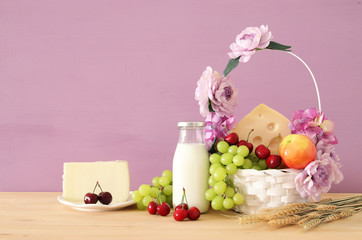 image of fruits and cheese in decorative basket with flowers over wooden table. Symbols of jewish holiday - Shavuot.