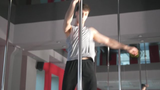 Athletic young man performing pole dance exercises in a studio