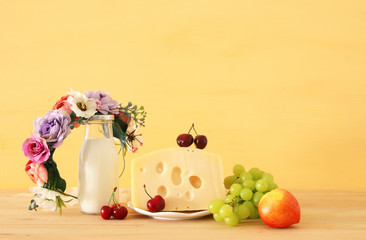 image of fruits and cheese in decorative basket with flowers over wooden table. Symbols of jewish holiday - Shavuot.