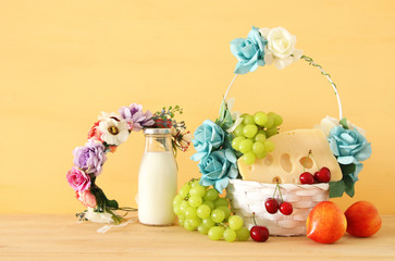image of fruits and cheese in decorative basket with flowers over wooden table. Symbols of jewish holiday - Shavuot.
