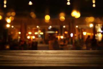 Image of wooden table in front of abstract blurred restaurant lights background.