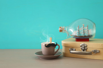Image of cup of coffee, old box and boat in the bottle over wooden table. Father's day concept.