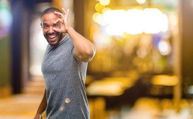 African american man with beard looking at camera through fingers in ok gesture. Imitating binoculars, beautiful eyes and smile at night