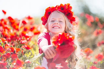 Beautiful blonde child girl is wearing wreath from red flowers in poppy meadow