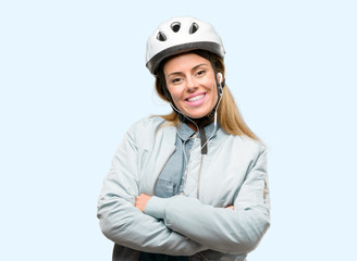 Young woman with bike helmet and earphones with crossed arms confident and happy with a big natural smile laughing