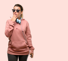 Naklejka premium Young sport woman with headphones and sunglasses looking at camera showing tong and making victory sign with fingers
