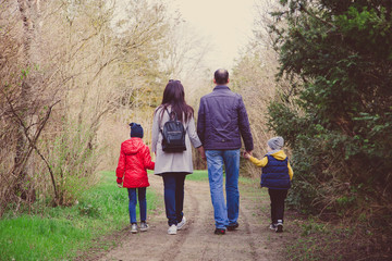 Happy young family spending time together outside in nature. parents holds the hands of a small children