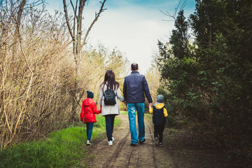 Happy young family spending time together outside in nature. parents holds the hands of a small children