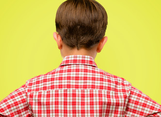 Handsome toddler child with green eyes backside, rear view over yellow background