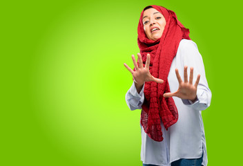Young arab woman wearing hijab disgusted and angry, keeping hands in stop gesture, as a defense, shouting