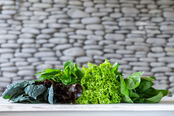 Leaves of green and red lettuce, kale, amaranth on white table with stone background