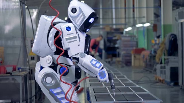 Human-like robot is working with a drill in a factory unit