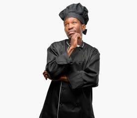 Young black cook wearing chef hat thinking and looking up expressing doubt and wonder