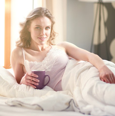 Obraz na płótnie Canvas Young woman drinking cup of coffee or tea while lying in bed.