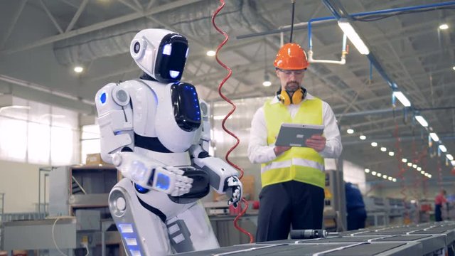 Male factory employee is switching a robot on after which it snads up and starts drilling