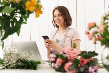 Cute cheerful florist lady using laptop computer chatting by mobile phone.