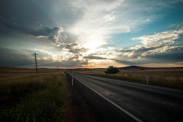 Road stretching into the horizon across vast grassy plains with spectacular sky. Australia