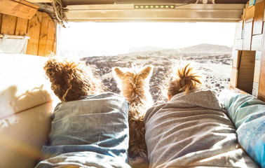 Hipster couple with cute dog traveling together on vintage van transport - Life inspiration concept with hippie people on minivan adventure trip watching sunset in love moment - Warm sunshine filter