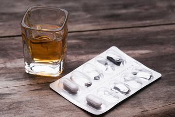 Whiskey or bourbon in a shot glass and pack of pills 