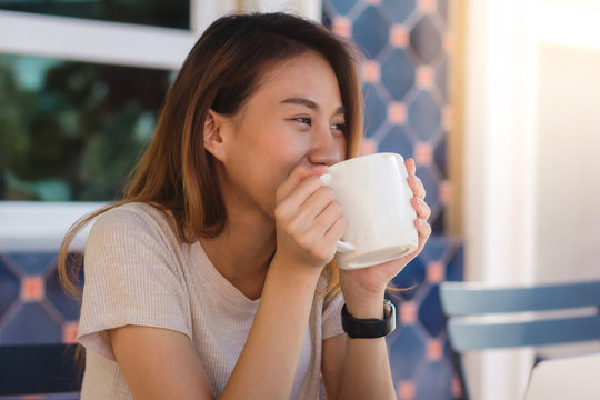 Portrait of happy young asian business woman with mug in hands drinking coffee in the morning at cafe. Asian women express emotion relax at the cafe or coffee shop. Woman food and drink cafe concept.