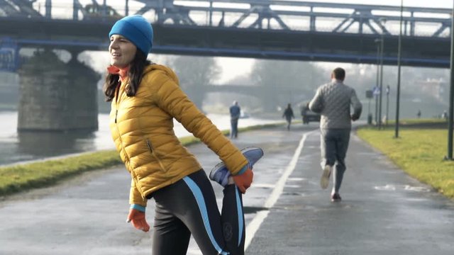 Sportive, young woman stretching body near river in city
