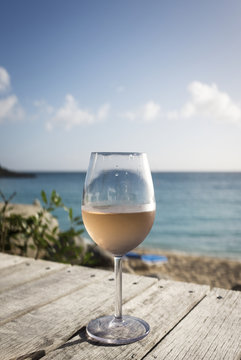 Glass of rose wine placed on wooden deck against the sea