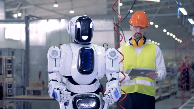Human-like robot starts working with a drill after a corresponding command from a factory worker
