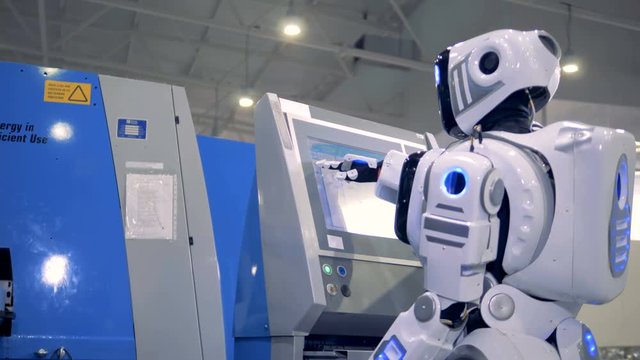 Human-like robot is coming to a control panel and setting parameters on a screen