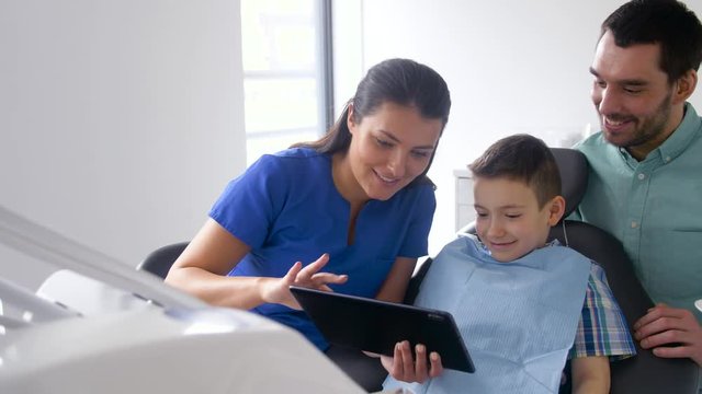 medicine, dentistry and healthcare concept - dentist showing tablet pc computer to father and son at dental clinic