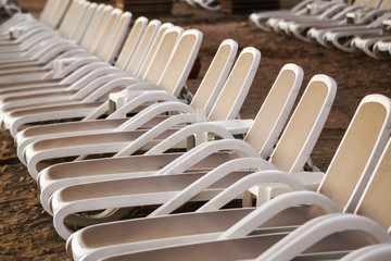 Row of white plastic deck chairs on a sandy beach close up