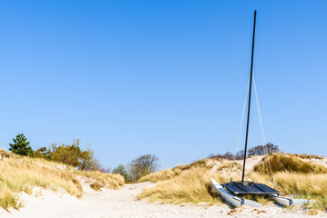 Falsterbo, Sweden - A catamaran sailboat resting on the sand dune of a beach on a sunny spring day.