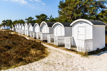 Obraz premium Falsterbo, Sweden - White seaside bathing huts in a row among heather and sand on a sunny warm day.