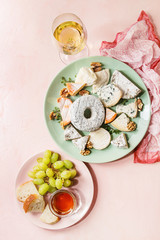 Cheese plate assortment of french cheese served with honey, walnuts, bread and grapes on turquoise ceramic plate and glass of white wine over pink pastel background. Top view, space.