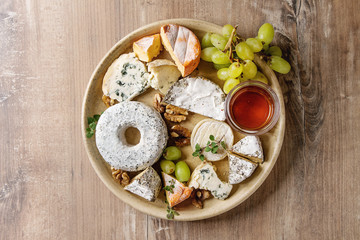 Cheese plate assortment of french cheese served with honey, walnuts, bread and grapes on ceramic plate over wood texture background. Top view, copy space.