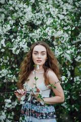 A beautiful girl in a dress stands next to a blooming cherry bush.