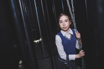 A little girl in school uniform in a dark room with hanging iron chains