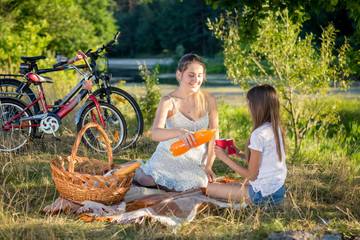 Cute teenage girl having picnic with mother in field at sunset