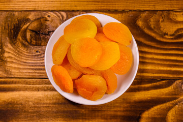Ceramic plate with dried apricots on wooden table. Top view