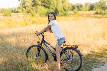 Fototapeta na wymiar Beautiful brunette girl riding mountain bike in field at sunset