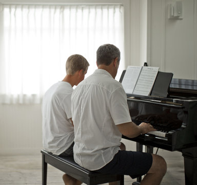 Mature adult man sitting at a piano with his teenage son.