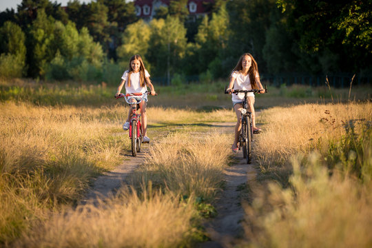 Two teenage girls riding on bicycles on the path at field