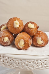 Front view, close up of five freshly baked, homemade lemon cream filled donuts on a white, round, display dish