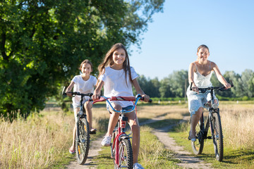 Portrait of three happy girls riding bicycles in field at sunny day