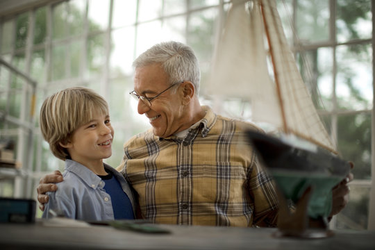 Smiling senior man with his hand on his grandsons shoulder as they stand next to a model boat.