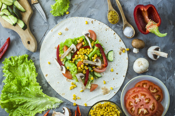 Mexican vegan burrito cooking - vegetables and mushrooms on tortillas on a gray kitchen table. Top view