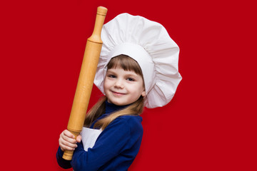 Happy little girl in chef uniform holds rolling pin isolated on red. Kid chef. Cooking Process Concept 