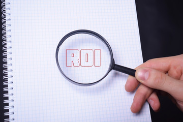 Businessman looking at a magnifying glass word:ROI
