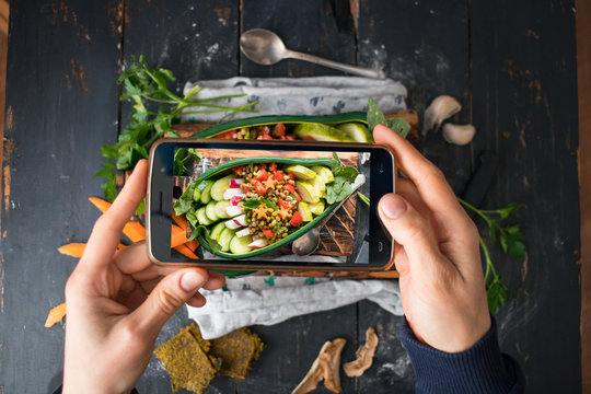 Phone photography of food. Woman hands take photo of lunch with smartphone for social media. Vegetables buddha bowl in avocado bowl. Raw vegan vegetarian healthy dinner 